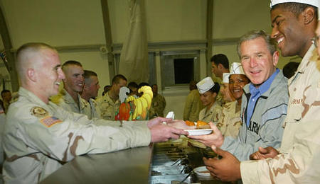 U.S. President George W. Bush helps serve U.S. troops dinner during his surprise visit for Thanksgiving at a military base at Baghdad International Airport, November 27, 2003.