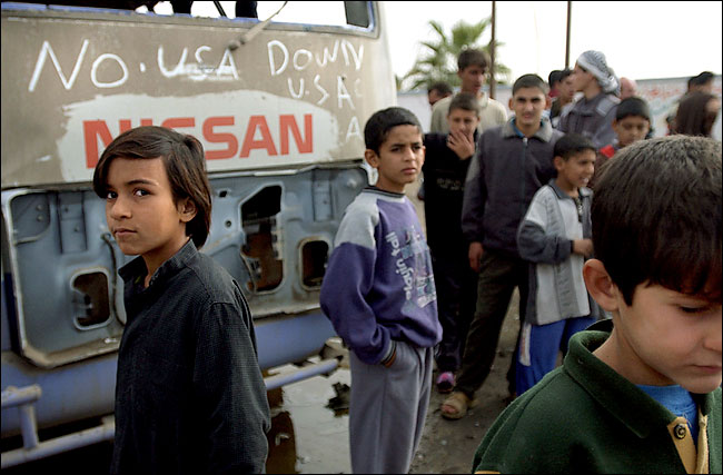 Children near a bus that was destroyed in fighting that killed as many as 54 insurgents and which American commanders vowed it would serve as a lesson, Samerra, central Iraq, November 30, 2003.
