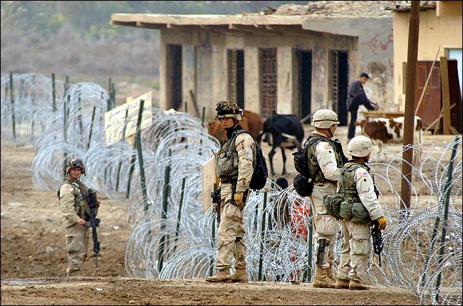 American soldiers on guard along a razor-wire fence that was put up around the Iraqi village of Abu Hishma in response to repeated attacks on troops by insurgents, early December 2003.
