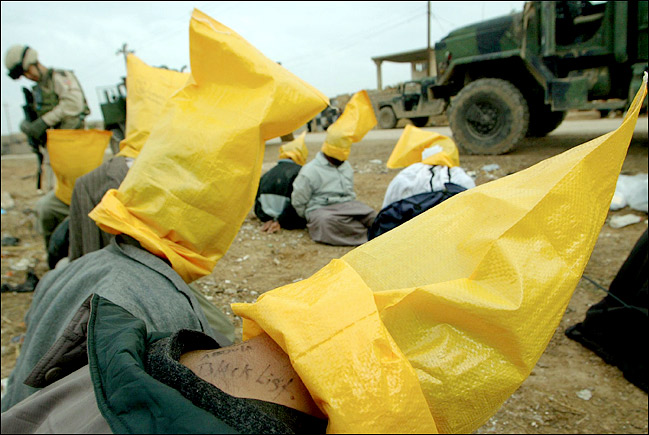 American soldiers of the 173rd Airborne Brigade guarded arrested prisoners whose heads were covered and notations made on their necks for use by intelligence officers during interrogation, Sunni Arab town of Hawija, northern Iraq, December 2, 2003.