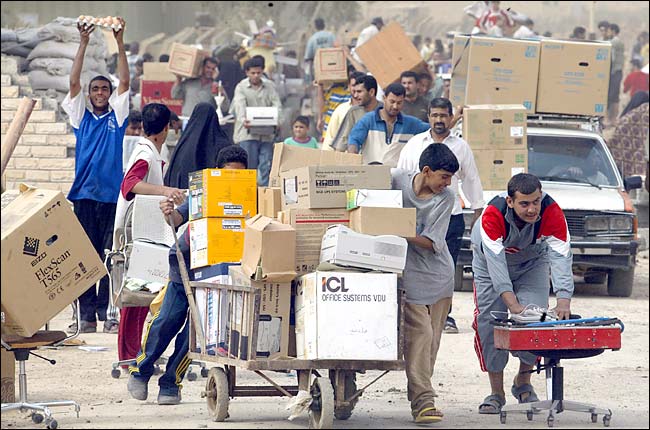 Iraqi civilians push carts loaded with goods after looting a government warehouse, a main road in southeastern Baghdad, April 9, 2003.