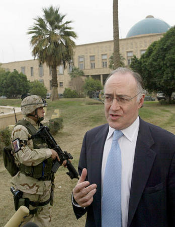 Britain's opposition leader Michael Howard, protected by a U.S. soldier, answers questions in the gardens of former Iraqi leader Saddam Hussein's palace, Baghdad, December 18, 2003.