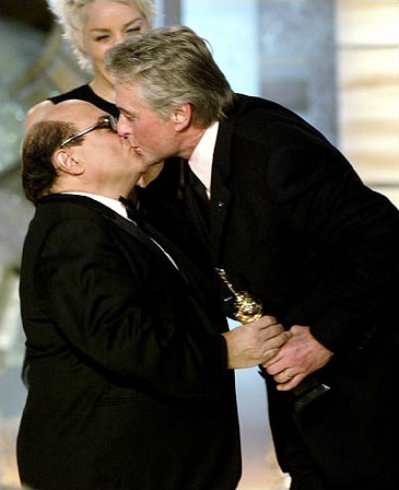 Actor Michael Douglas plants a kiss on actor Danny DeVito after Douglas accepted the Cecil B. DeMille Award during the annual Golden Globe Awards, January 25, 2004.