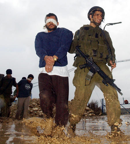 Israeli soldiers guard blindfolded Palestinian militants at the Erez border crossing who were arrested during an army operation in the Gaza Strip, February 11, 2004.