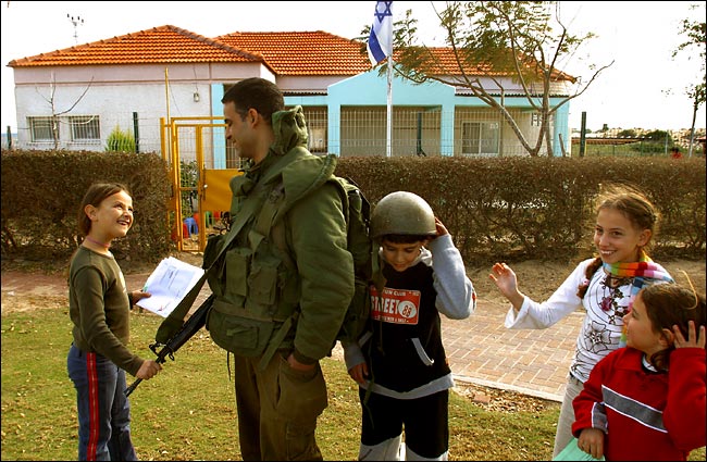 An Israeli soldier carries out his reserve duty guarding the kindergarten and children on the playground, the settlement of Gush Qatif, Gaza, Israel, February 2004.