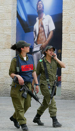 Israeli female soldiers walk next to a clothing advertisment, one of them wearing a vest reading in Hebrew 'at the service of the police,' as they patrol after the killing by Israel of Hamas spiritual leader Ahmed Yassin in a helicopter missile strike in Gaza city, downtown Jerusalem, March 23, 2004.