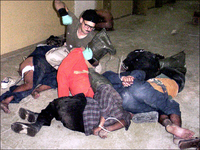 Unidentified American soldier appeared to be poised to punch an Iraqi detainee amid others who lay bound at the hands and feet, undated photo from the Abu Ghraib prison near Baghdad.