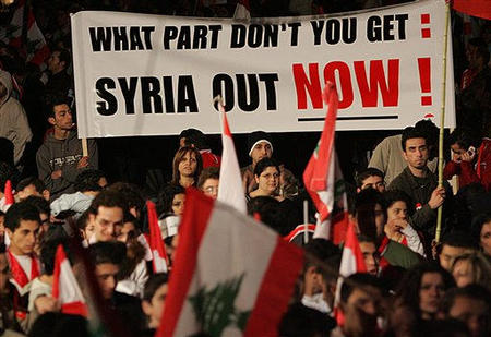 Lebanese protesters carry an anti-Syrian banner as they watch the live TV broadcast of a speech by Syrian President Bashar al-Asad on a giant screen set up in the Martyrs square in central Beirut, Lebanon, March 5, 2005.