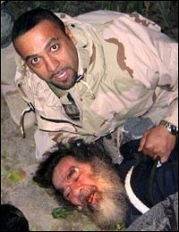 The deposed Iraqi dictator Saddam Hussein held down by an American soldier, whose face has been deliberately obscured, after he was dragged from his hiding place, an 8ft hole in the ground. The dictator was captured on Decrmber 13, 2003 at a house on the outskirts of his home town, Tikrit, north of Baghdad. The picture purporting to show the capture of appeared on the internet site Shock and Awe - Military.com on January 7, 2003 and a version revealing the face of the American soldier appeared later in The Sun tabloid.
