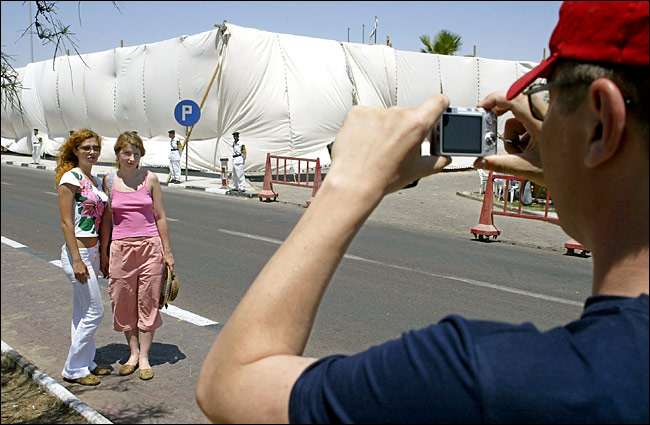 Just a day after the explosions, tourists, undeterred by terrorist attacks, take photos in front of a destroyed hotel now masked in cloth, Sharm A-Sheik, July 25, 2005.
