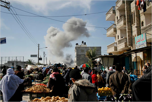 On the eighteenth day of Israel’s war against Gaza, Palestinians buy food in the street as smoke rose following explosions caused by Israeli military operations, Rafah, January 13, 2009.