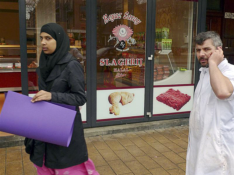 A butcher talks on his mobile phone as a veiled woman passes a so-called Halal butchers store, Amsterdam, Netherlands, March 31, 2011.
